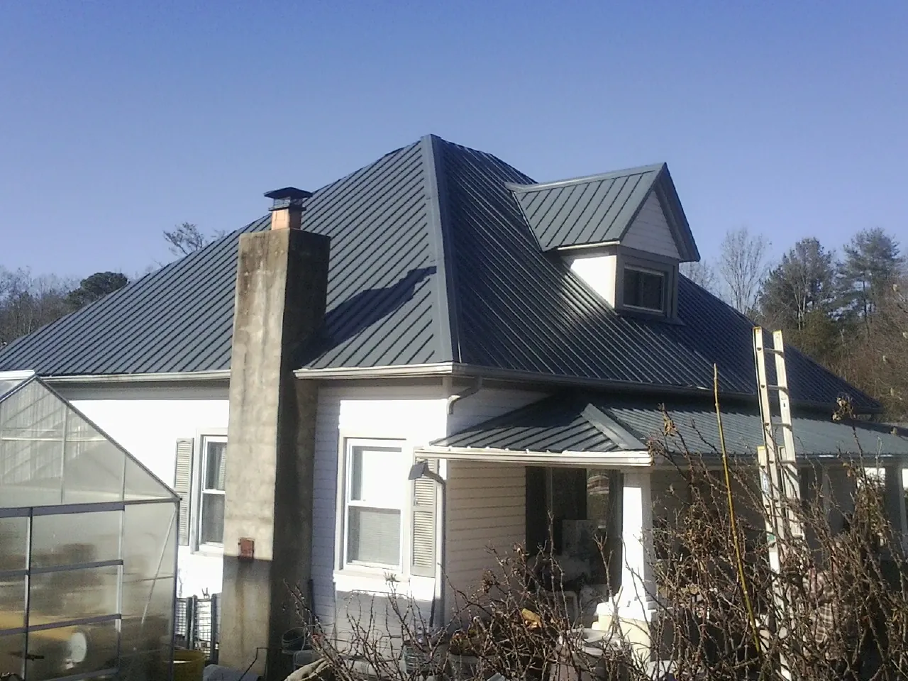 Dark blue standing seam metal roof on a white farmhouse with dormer — Slate & Tile Roof Repair by Roofing Brothers in Ellettsville