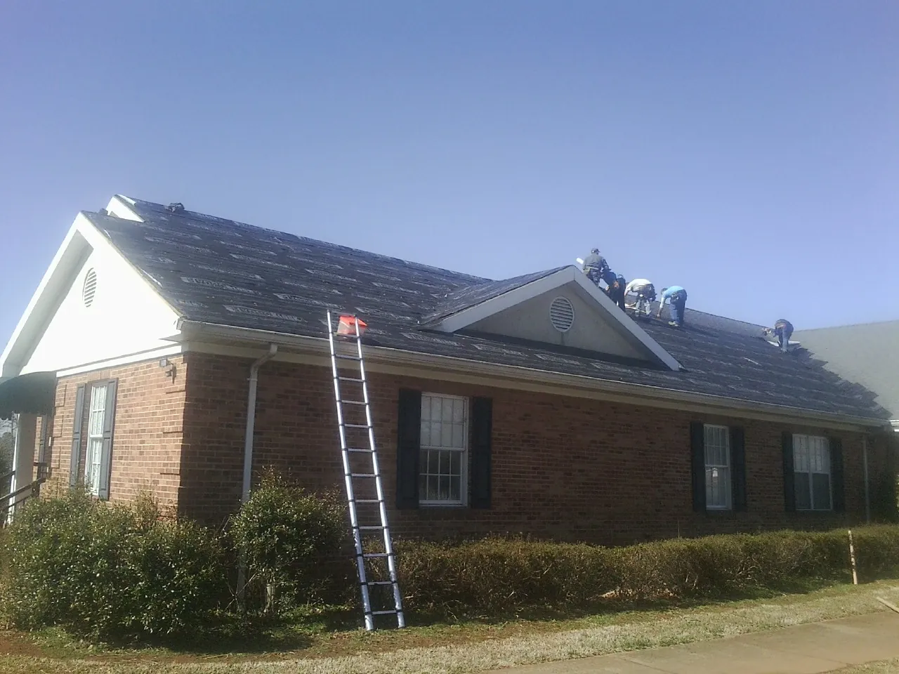 Crew tearing shingles off a brick ranch roof with a ladder set — Metal Roof Repair work by our crew in Ellettsville