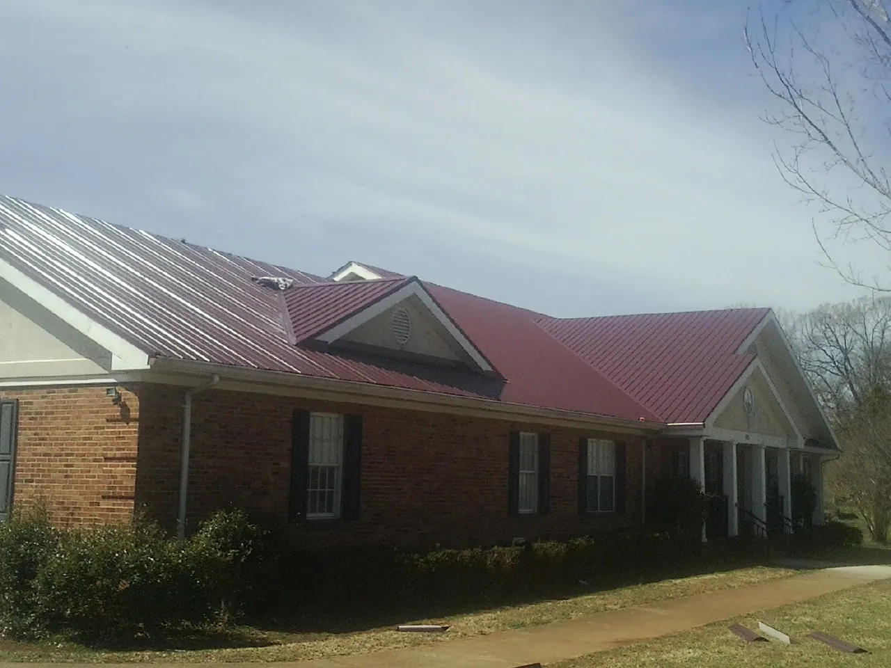 Red metal roof with gabled entries on a long brick building, from a Hail Damage Roof Repair job in Ellettsville