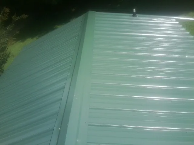 New green metal panels meeting at the ridge of a roof — Flat Roof Repair work by our crew in Ellettsville