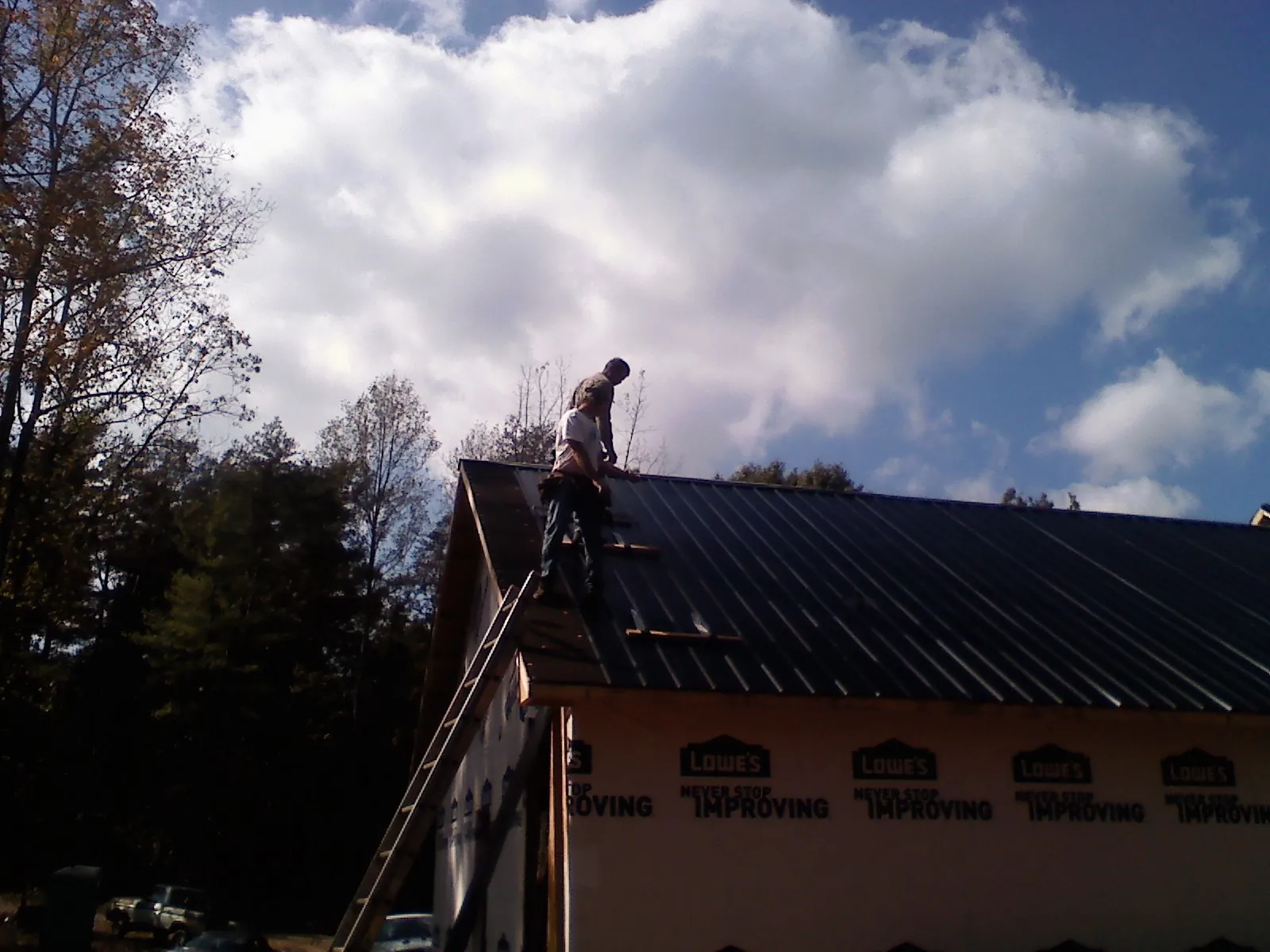 Roofer fastening dark metal panels high against a cloudy sky, from a Roof Inspection job in Ellettsville