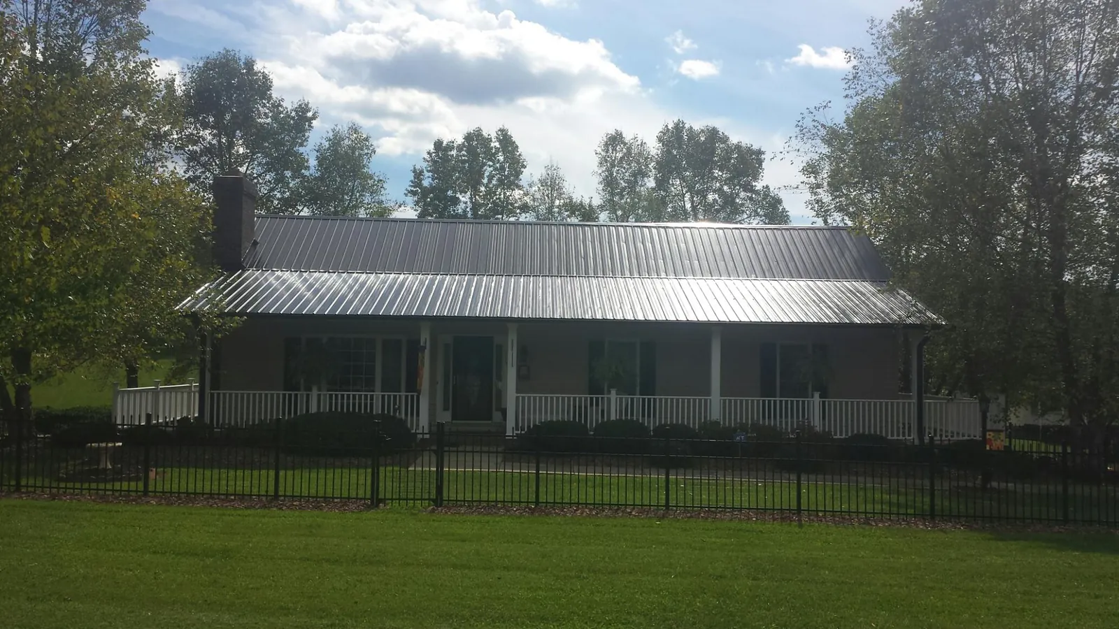 Gray metal roof on a brick ranch with a full width front porch — Gutter Guard Installation work by our crew in Ellettsville