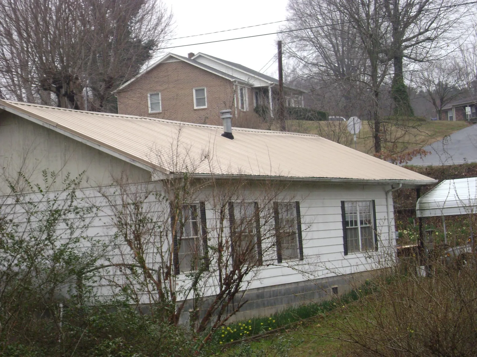 Tan metal roof on a white sided house set into a hillside — Commercial Roofing by Roofing Brothers in Ellettsville