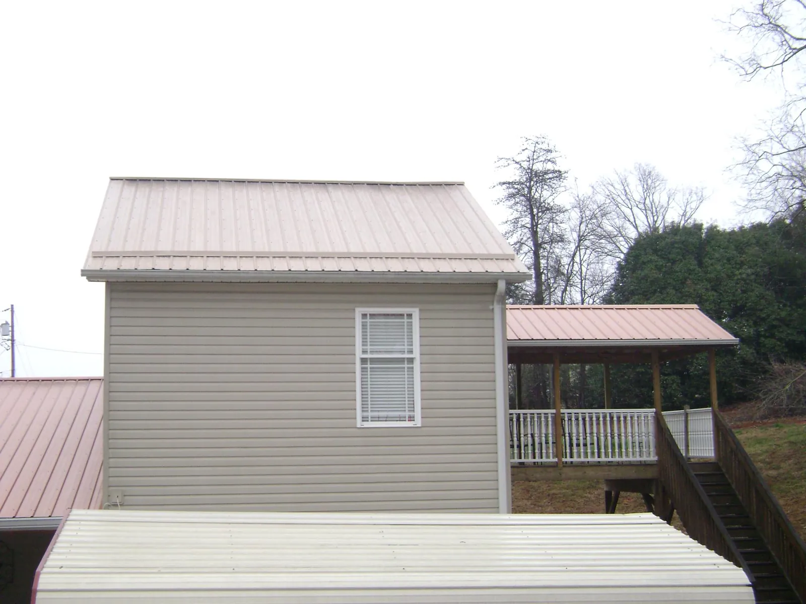 Tan metal roofs on a two story addition and attached porch, from a Roof Replacement job in Ellettsville